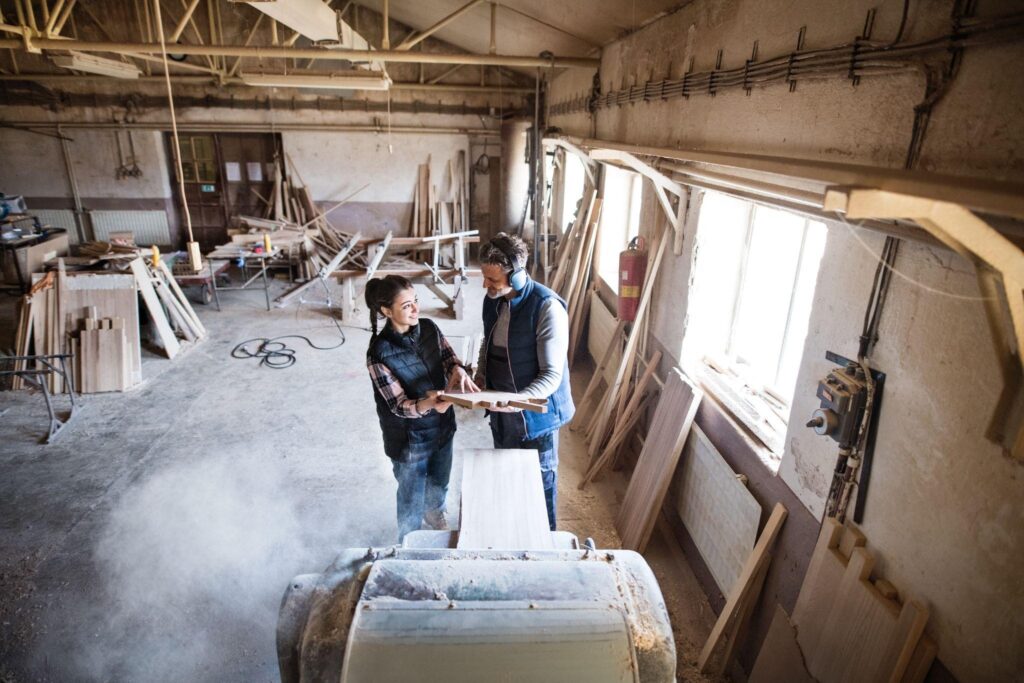 Two barn restoration specialists working on custom wood repairs inside a workshop, using traditional craftsmanship techniques to preserve historic barns.