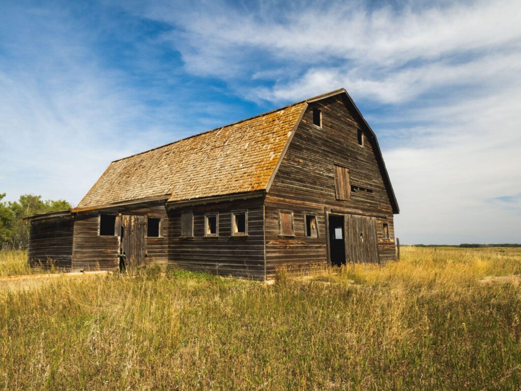 Rustic wooden barn with a sagging roof in an open field—ideal example for barn restoration companies or barn repair contractors near me.