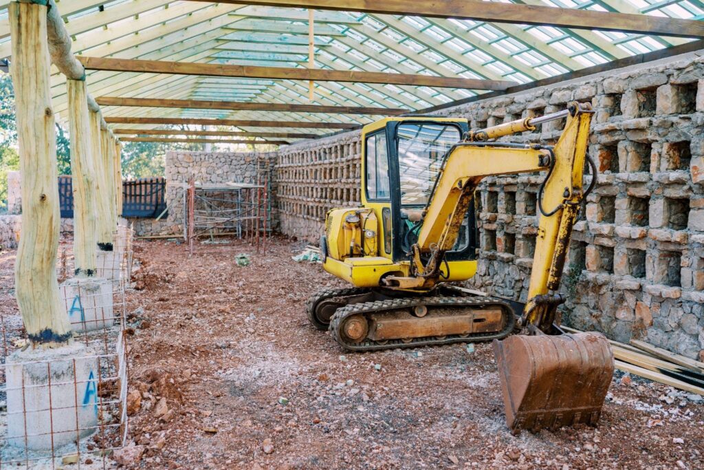 Yellow excavator inside a partially restored barn structure on a farm, showcasing professional barn restoration in New York.