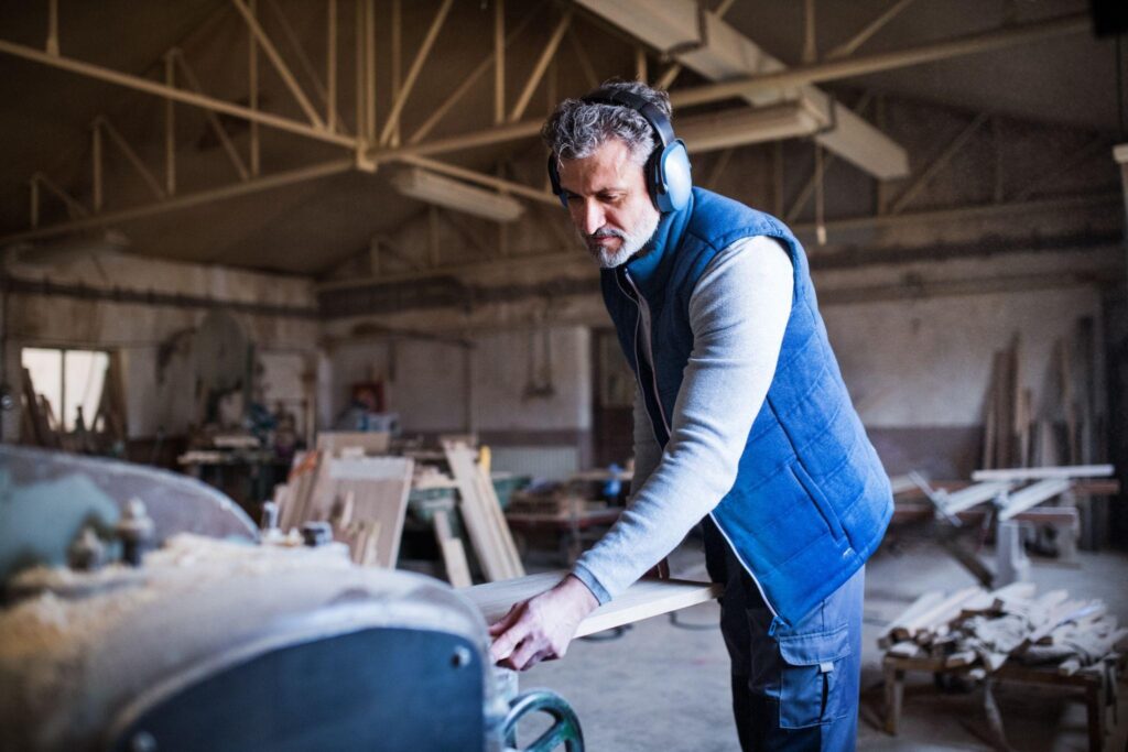 Skilled barn restoration contractor sanding reclaimed wood in a carpentry workshop near Pennsylvania.