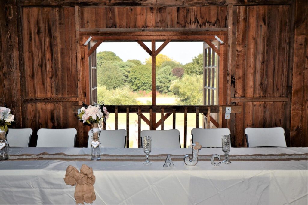 Barn event space with a head table, flowers, and open doors to green fields. Shows barn conversion for events.