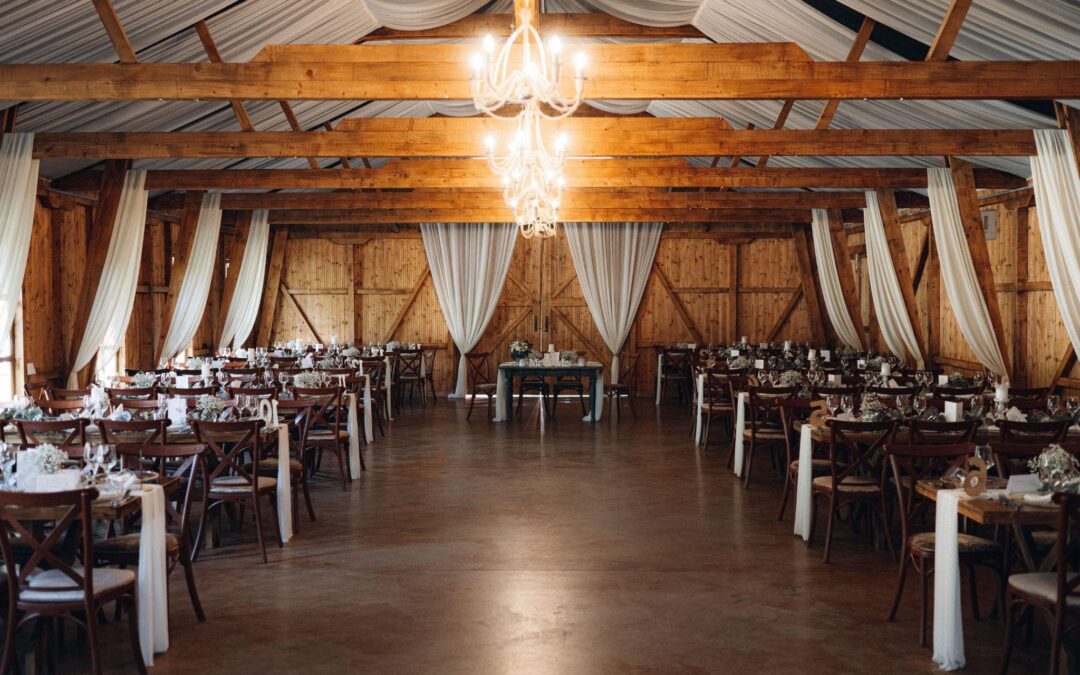 Rustic barn wedding venue with wood beams, chandeliers, and rows of tables. A perfect example of barn construction near you for events.