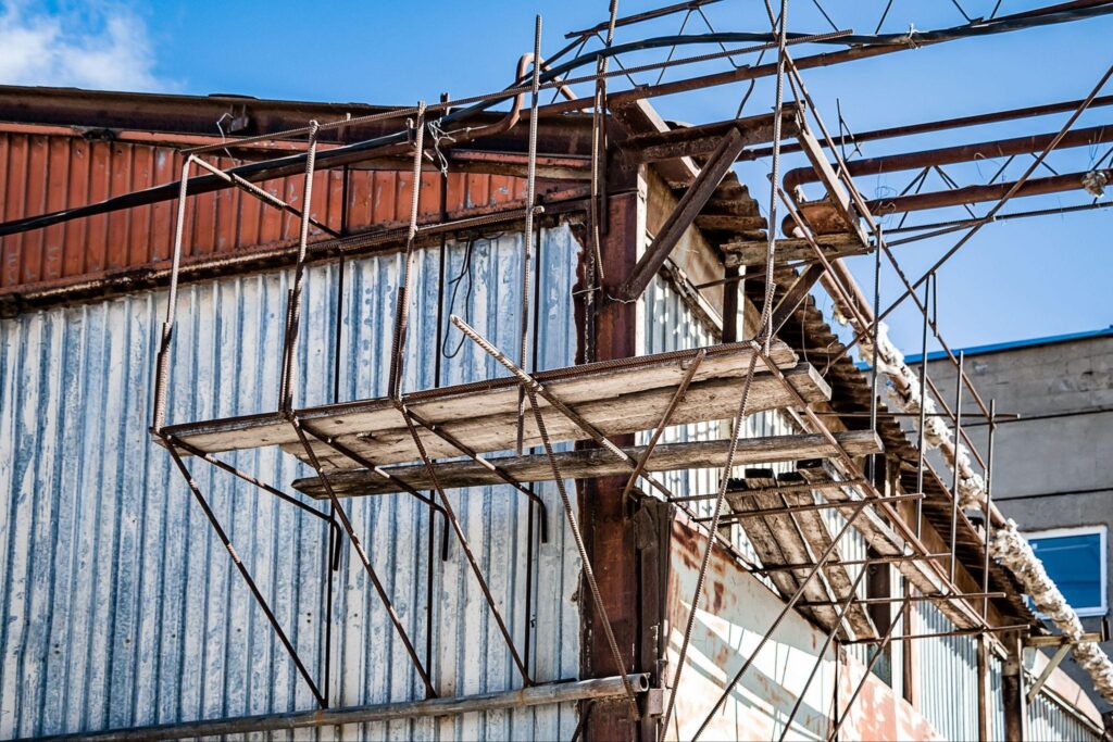 Close-up of rusty scaffolding and partial metal siding on an industrial structure during barn repair work.