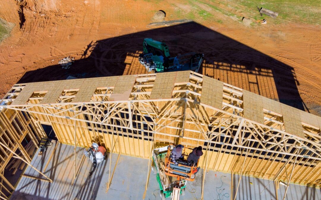 Workers installing roof trusses on new pole barn framing, how to build a pole barn with a strong foundation and reinforcements in New York.