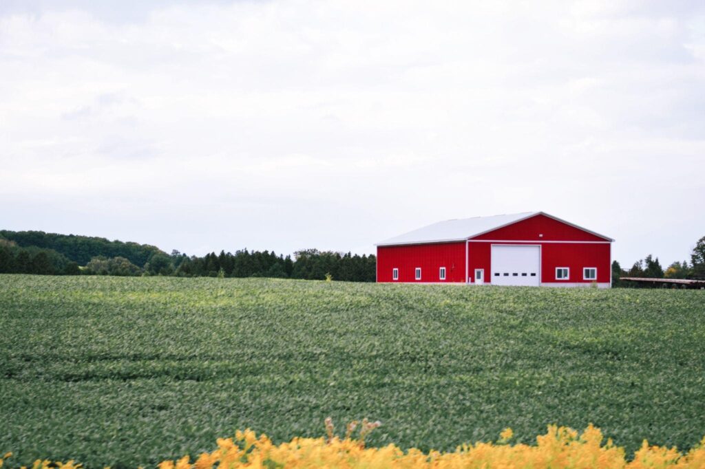 Red barn with large sliding barn door styles on a New York farm surrounded by green fields.