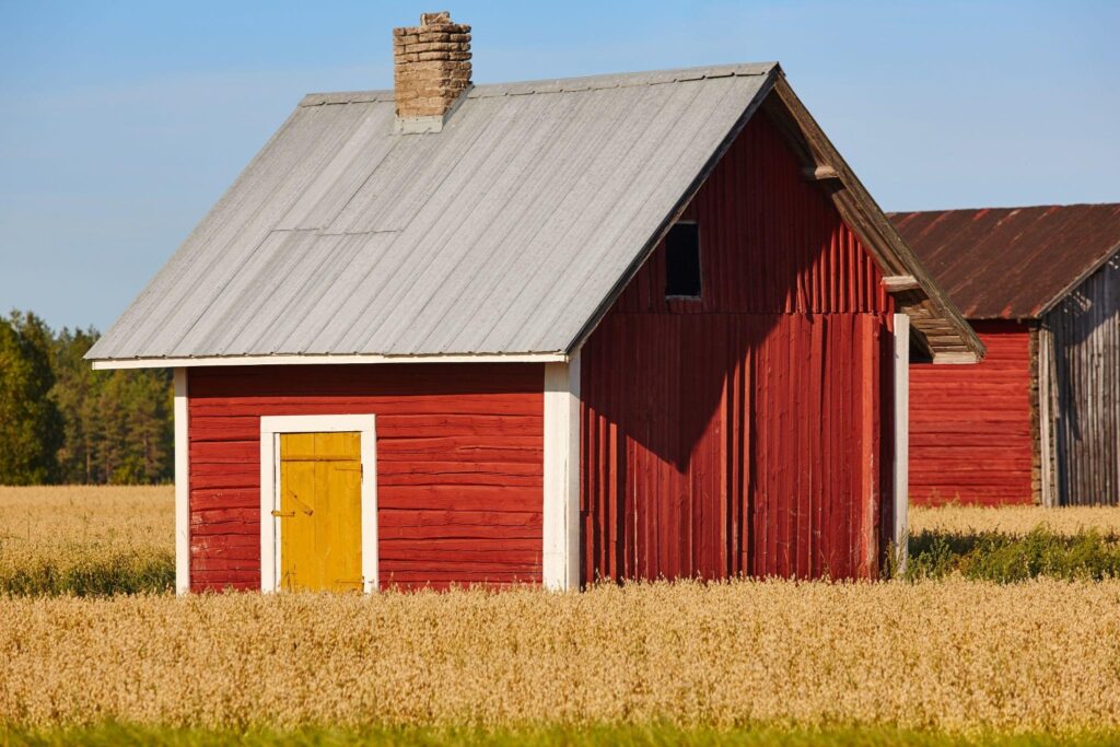 Classic red barn with yellow door in a New York field, showcasing traditional barn paint colors on wood siding and a metal roof.