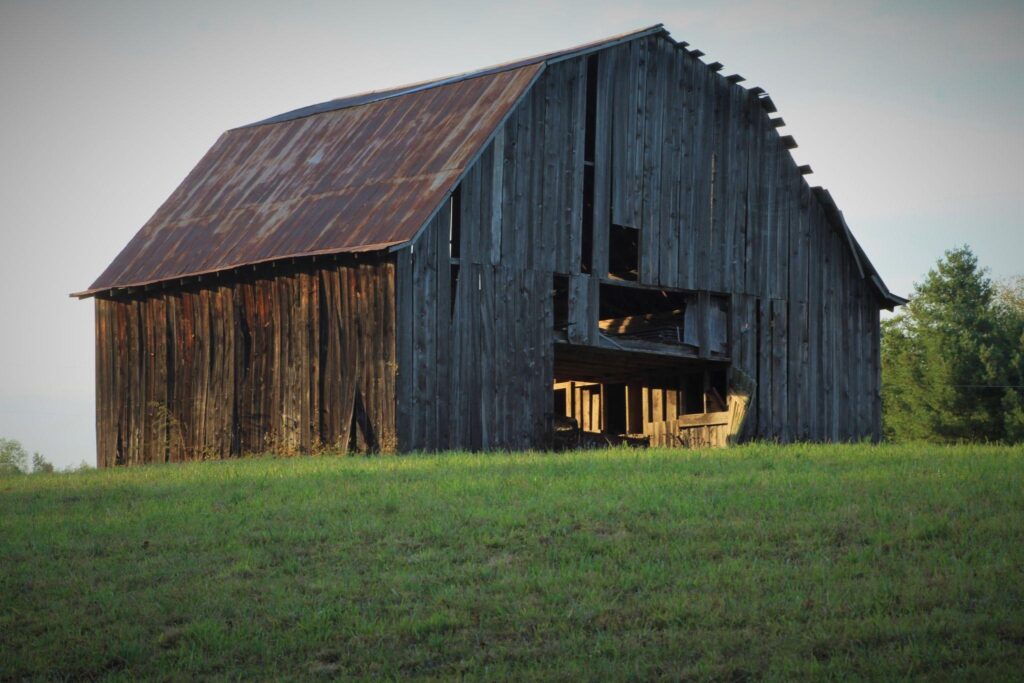 Old barn restoration ideas for New York farms showing a weathered wooden barn with a rusted roof at sunset.