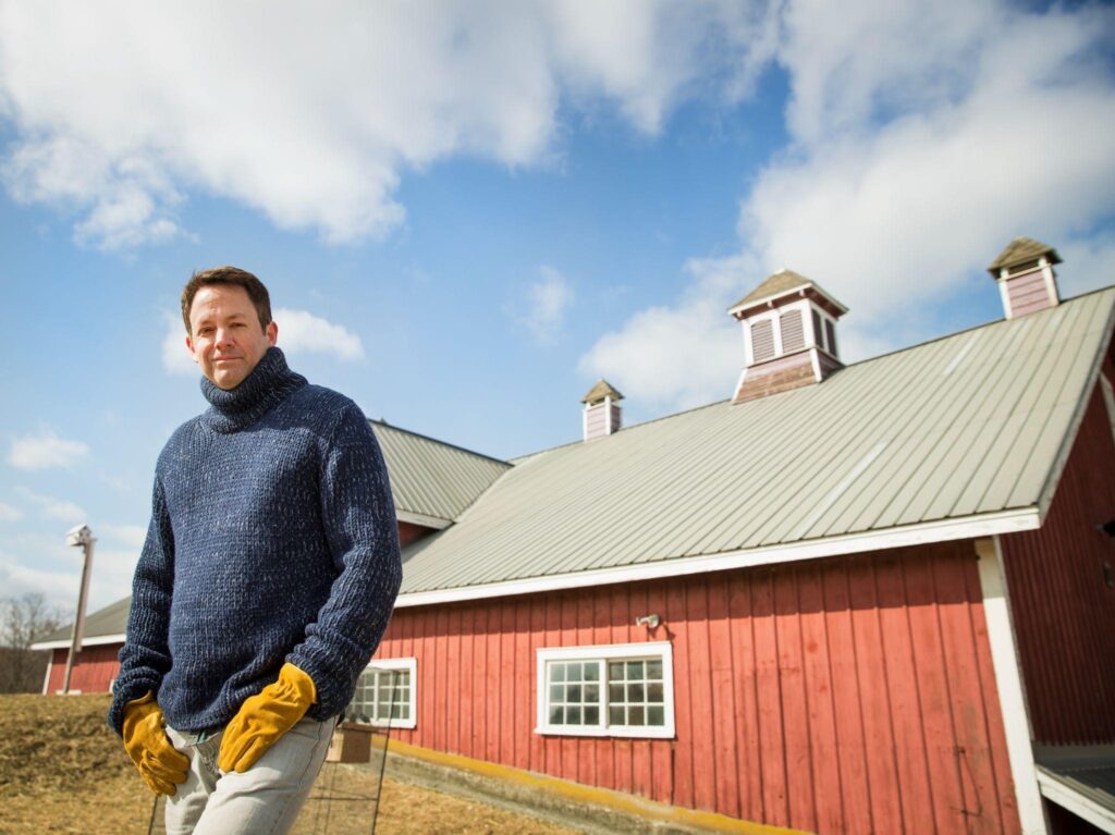 Homeowner standing beside a restored red barn with a pole barn roof in Cold Spring, New York, symbolizing expert barn restoration and care.