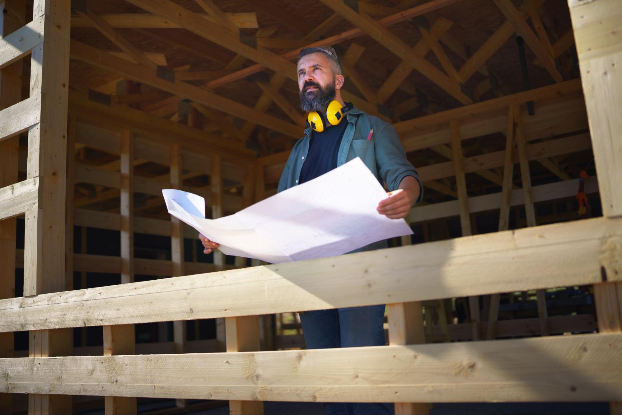 Contractor reviewing blueprints inside a pole barn frame during construction in New York